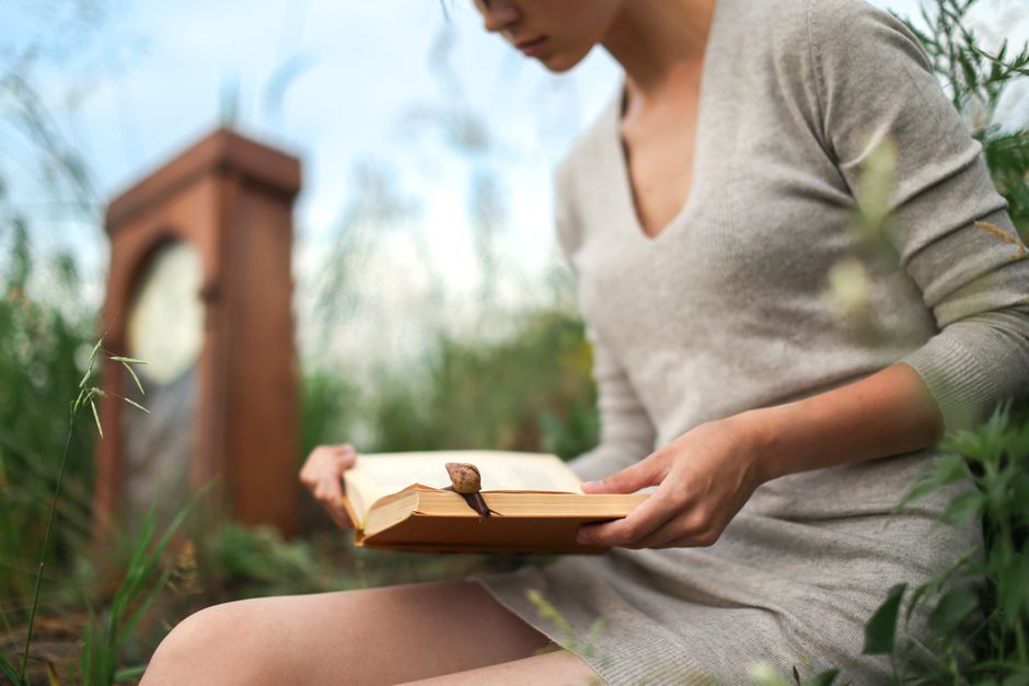 A woman reading a book outdoors amid green nature, symbolizing relaxation and leisure.